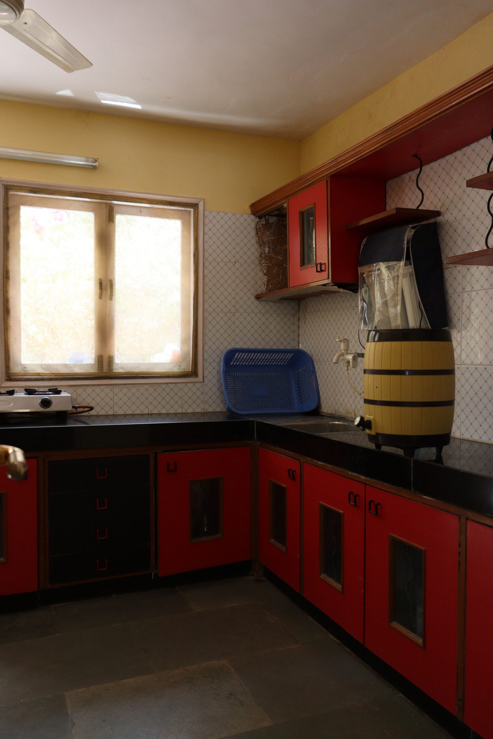 Cozy Indian kitchen featuring vibrant red cabinets, a window, and a water barrel.